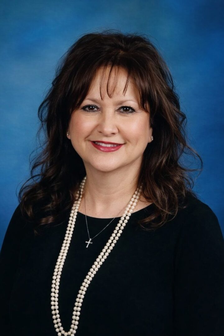 Smiling woman with pearl necklace, blue background.